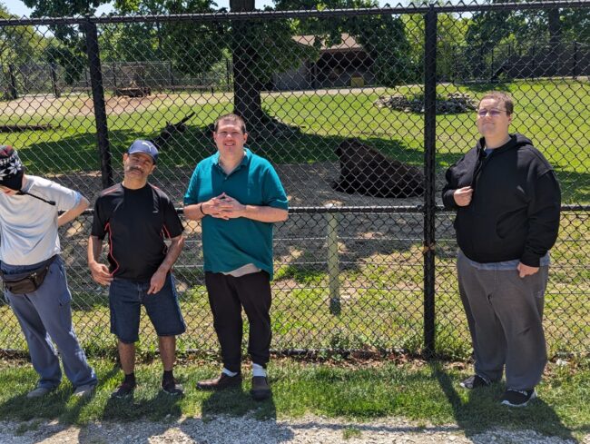 Men posing by a fence containing a bison at a zoo