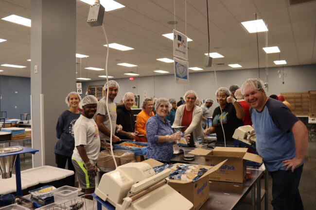 IMG_4624 Individuals posing for a picture while volunteering making rice meal packs at Feed My Starving Children