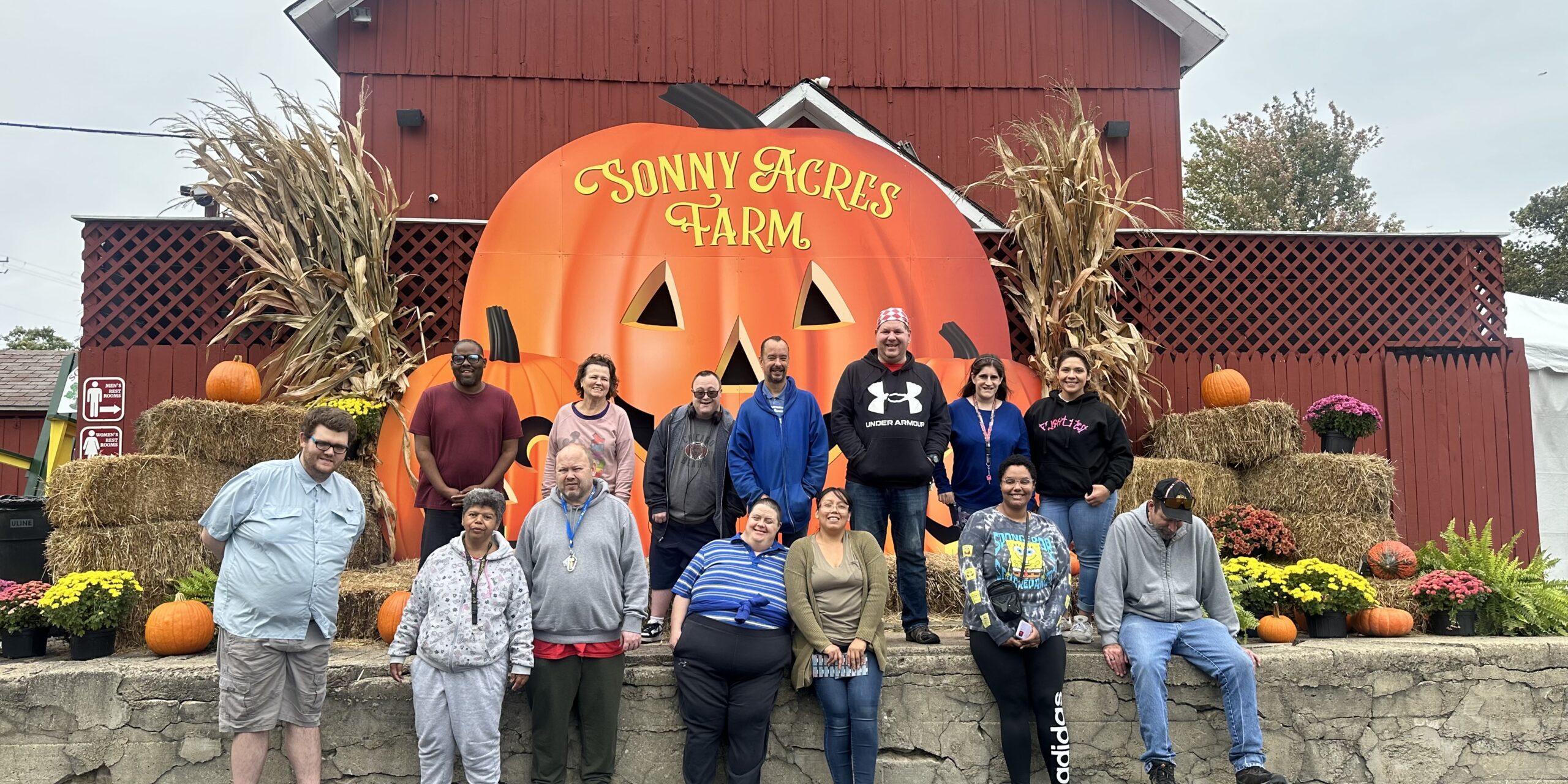 Individuals posing in with a giant pumpkin sign in front of a big red barn
