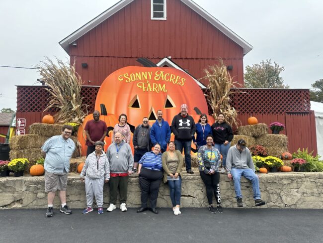 Individuals posing in with a giant pumpkin sign in front of a big red barn