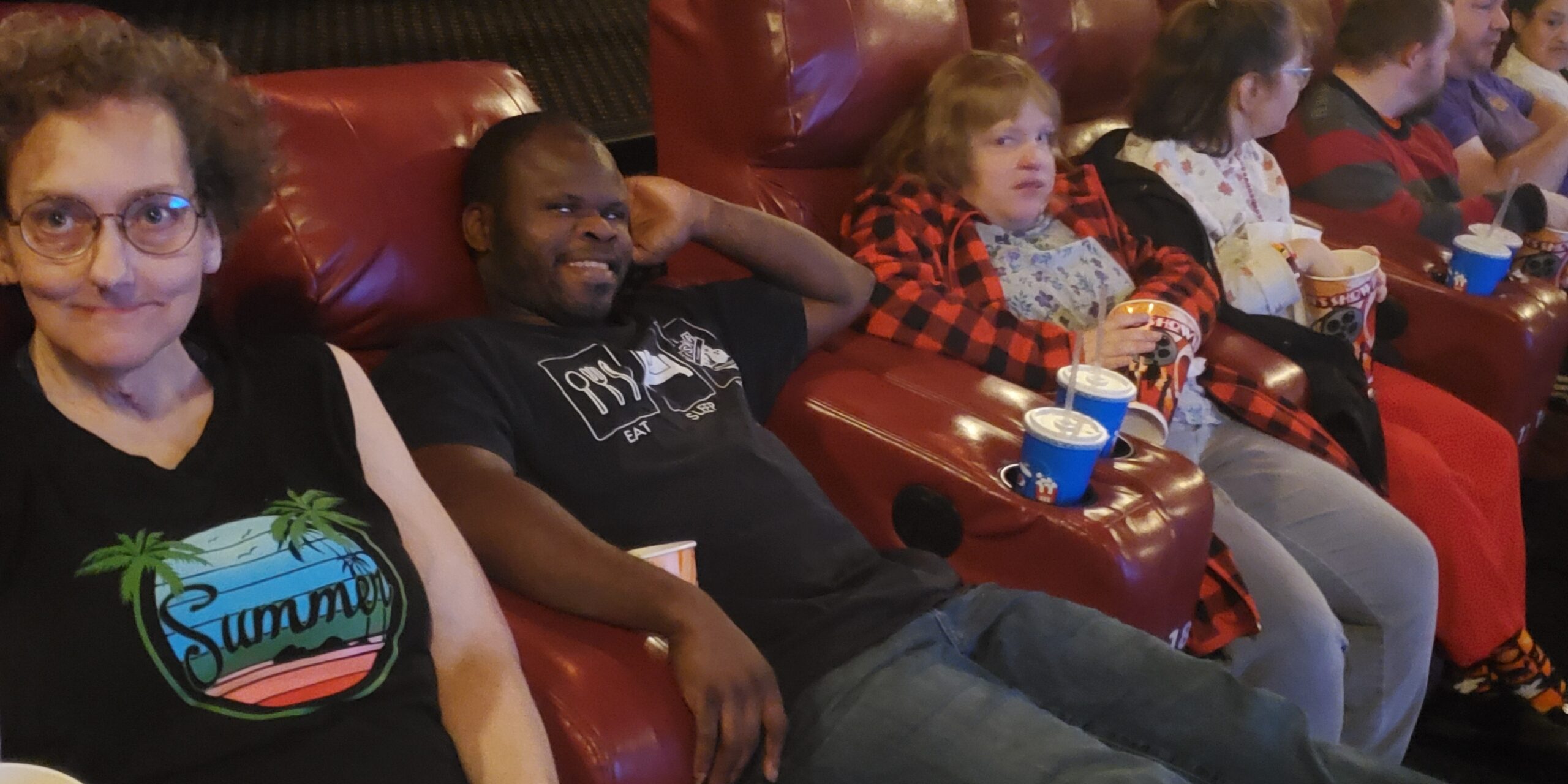 Individuals relaxing with popcorn and drinks in movie theater chairs