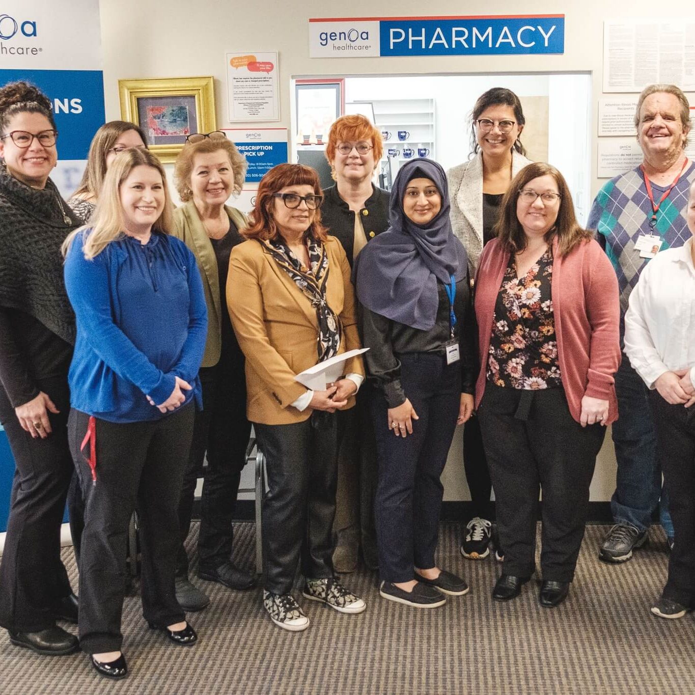 A group of individuals smiling in-front of a pharmacy