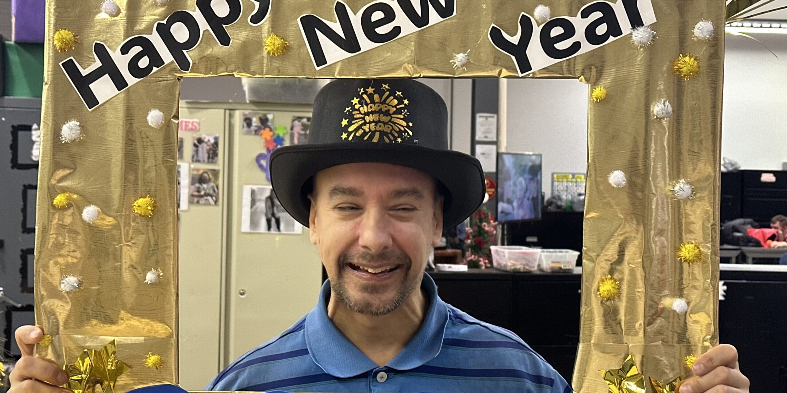 Individual smiling while holding a gold "Happy New Year 2025" photo frame