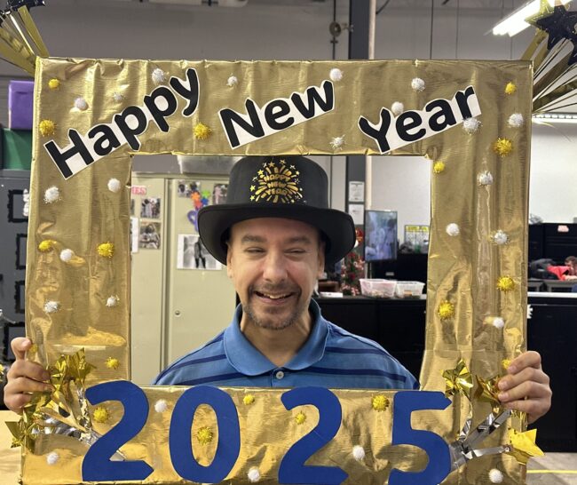 Individual smiling while holding a gold "Happy New Year 2025" photo frame