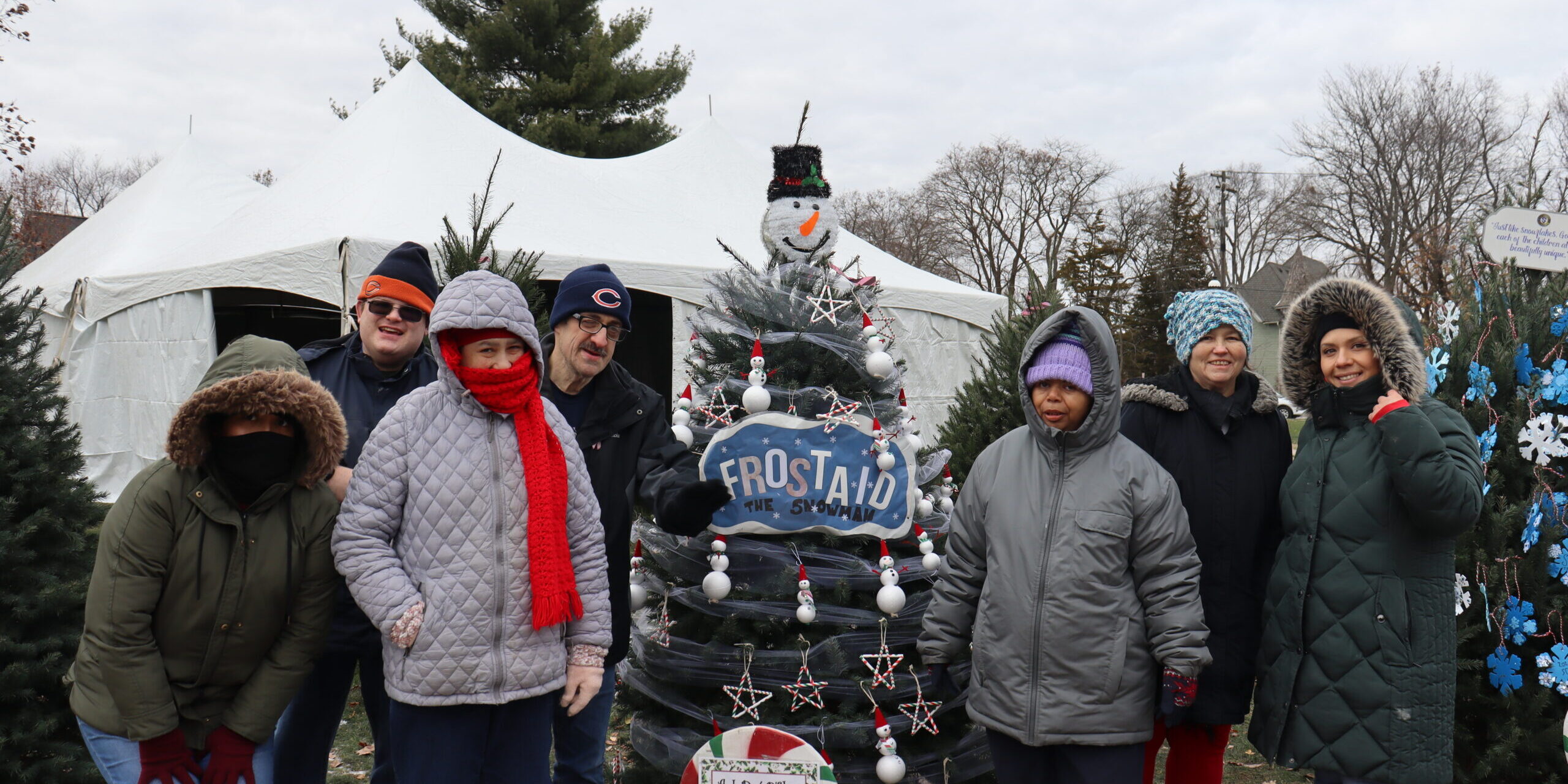A group of individuals posing in front of the "Frost-AID the Snowman" Christmas Tree