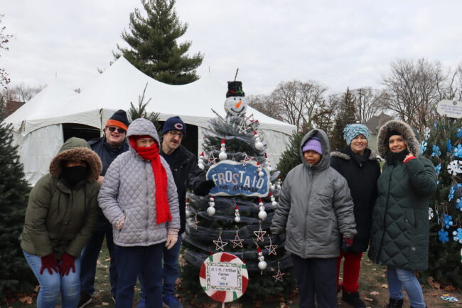 A group of individuals posing in front of the "Frost-AID the Snowman" Christmas Tree