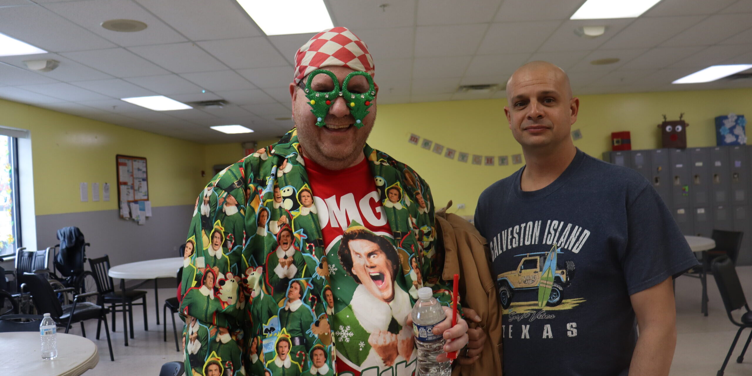 Man decked out in Elf clothing and upside-down Christmas tree glasses poses with another man
