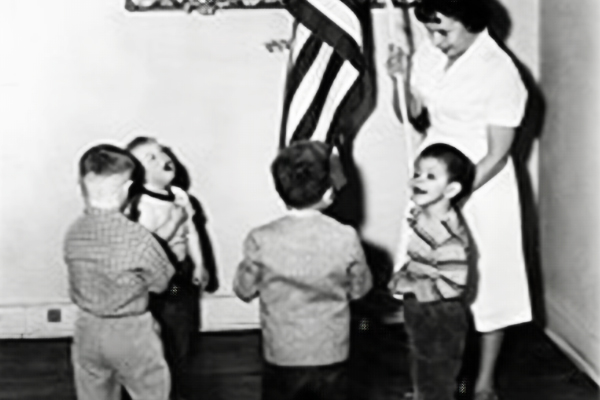 School teacher holding American Flag while four students hold their hands over their hearts