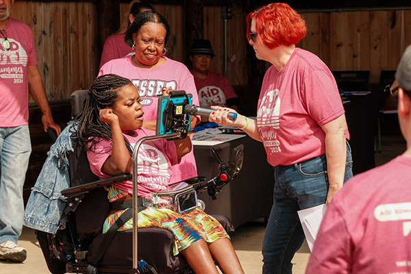 Woman holding microphone to a woman in a wheelchair's assisted communication device